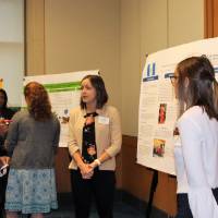A group of attendees standing around another poster presentation, asking questions